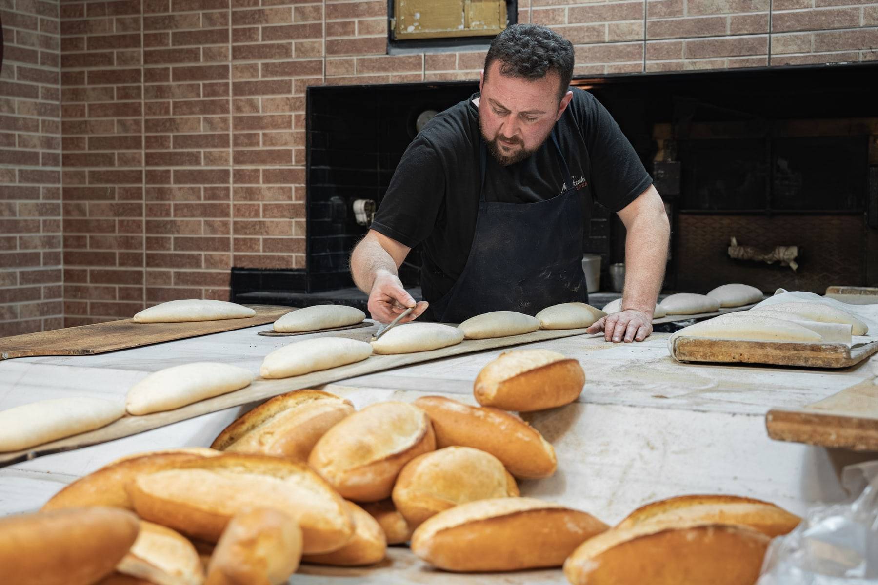 Un boulanger façonne les pâtons devant le four, des pains dorés au premier plan.