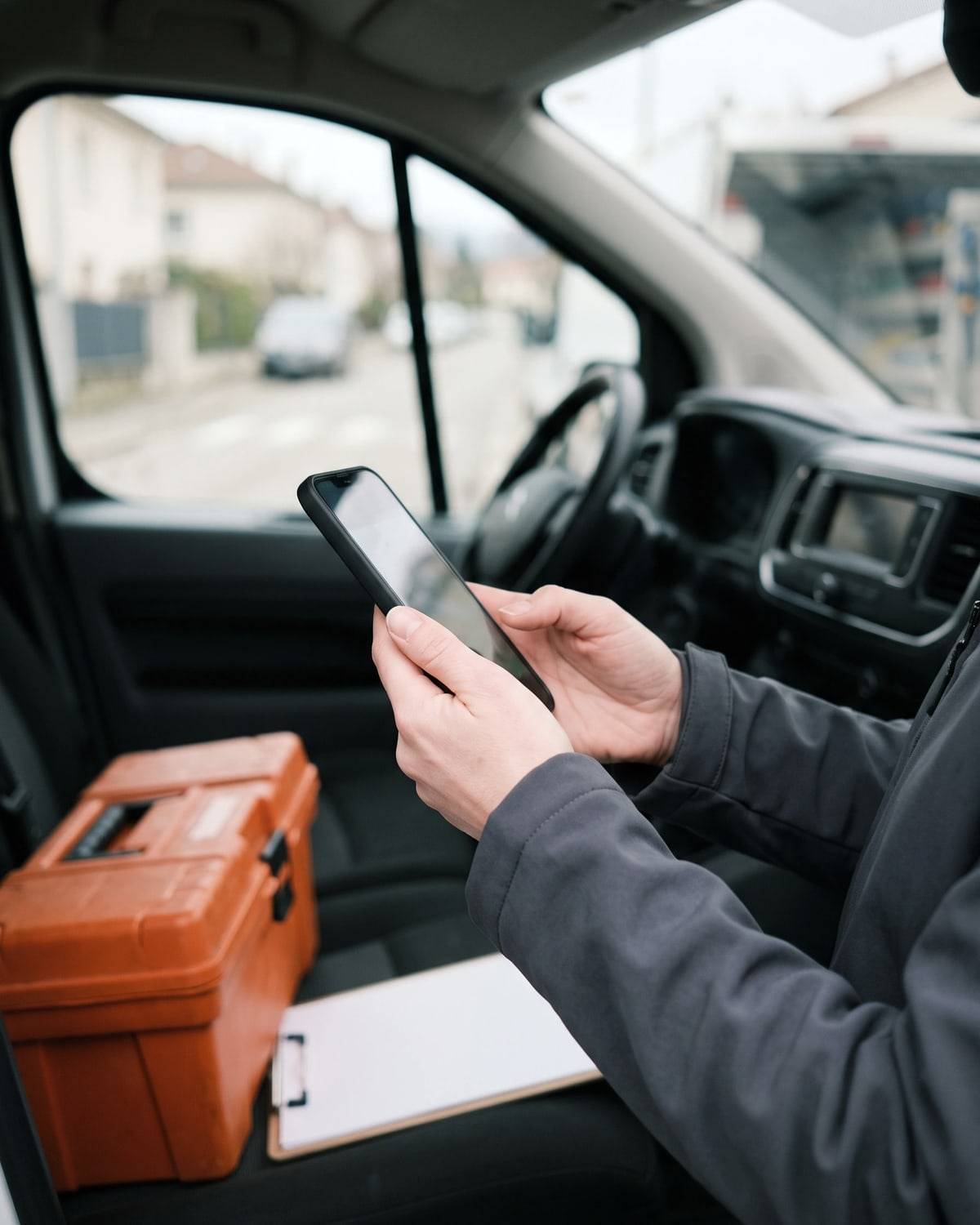 Dans son camion, entre deux interventions, un plombier tient son téléphone, la caisse à outils sur le siège.
