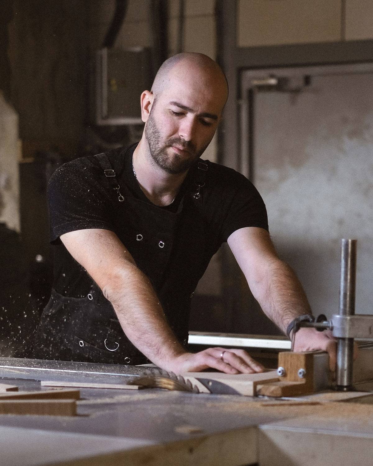 Un menuisier pousse une planche sur sa scie, dans son atelier.