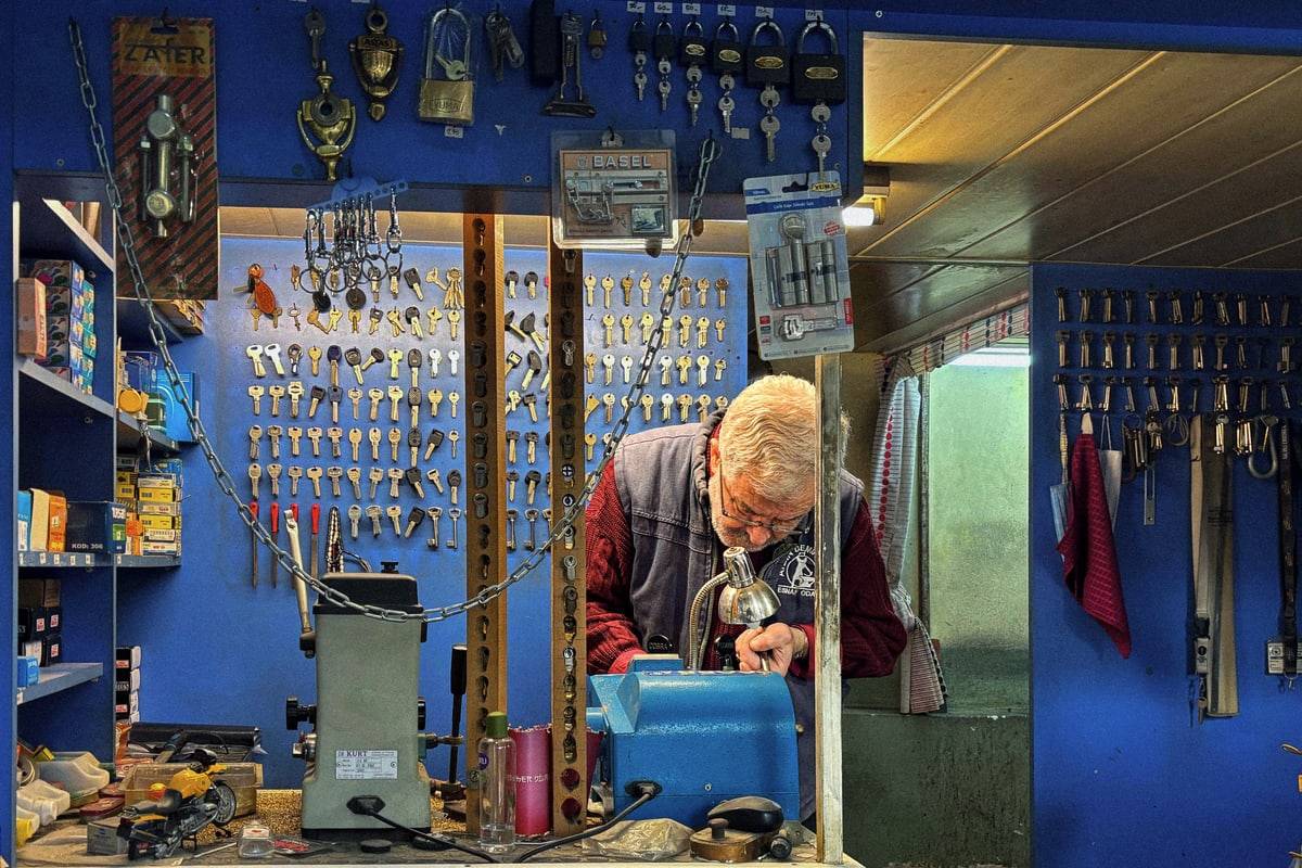 Un serrurier taille une clé dans sa boutique aux murs couverts de clés.