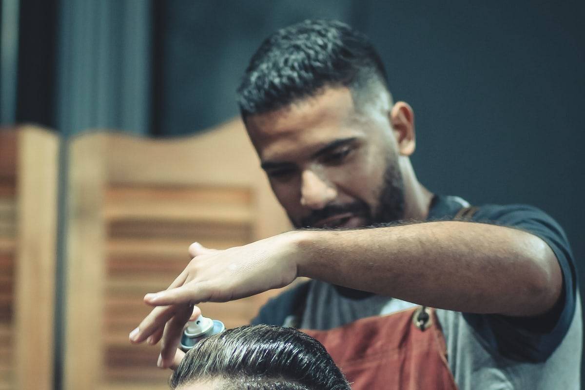 Un barbier en tablier de cuir met la coupe d'un client en forme, une bombe de laque à la main.