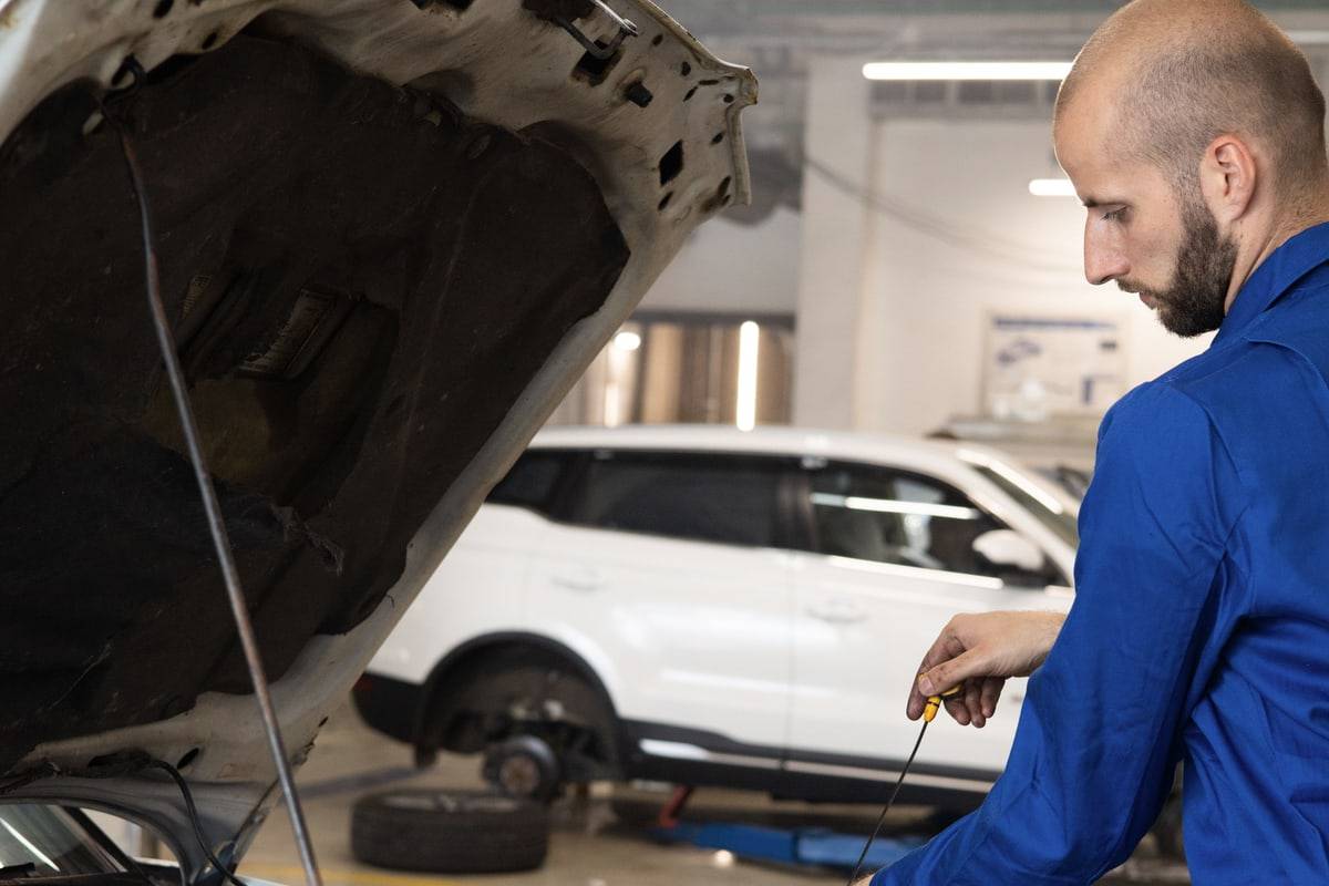 Un mécanicien vérifie le niveau d'huile, capot ouvert, dans un atelier.
