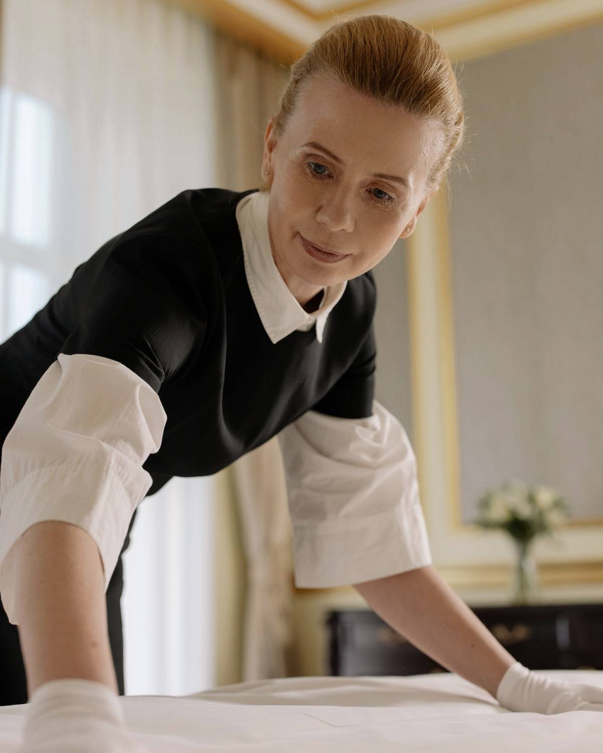 Une femme de chambre lisse les draps d'un lit d'hôtel.