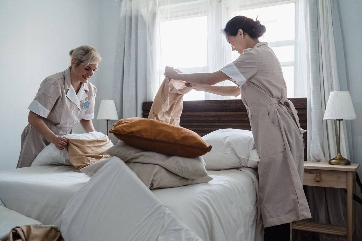 Deux femmes de chambre préparent le lit d'une chambre d'hôtel.