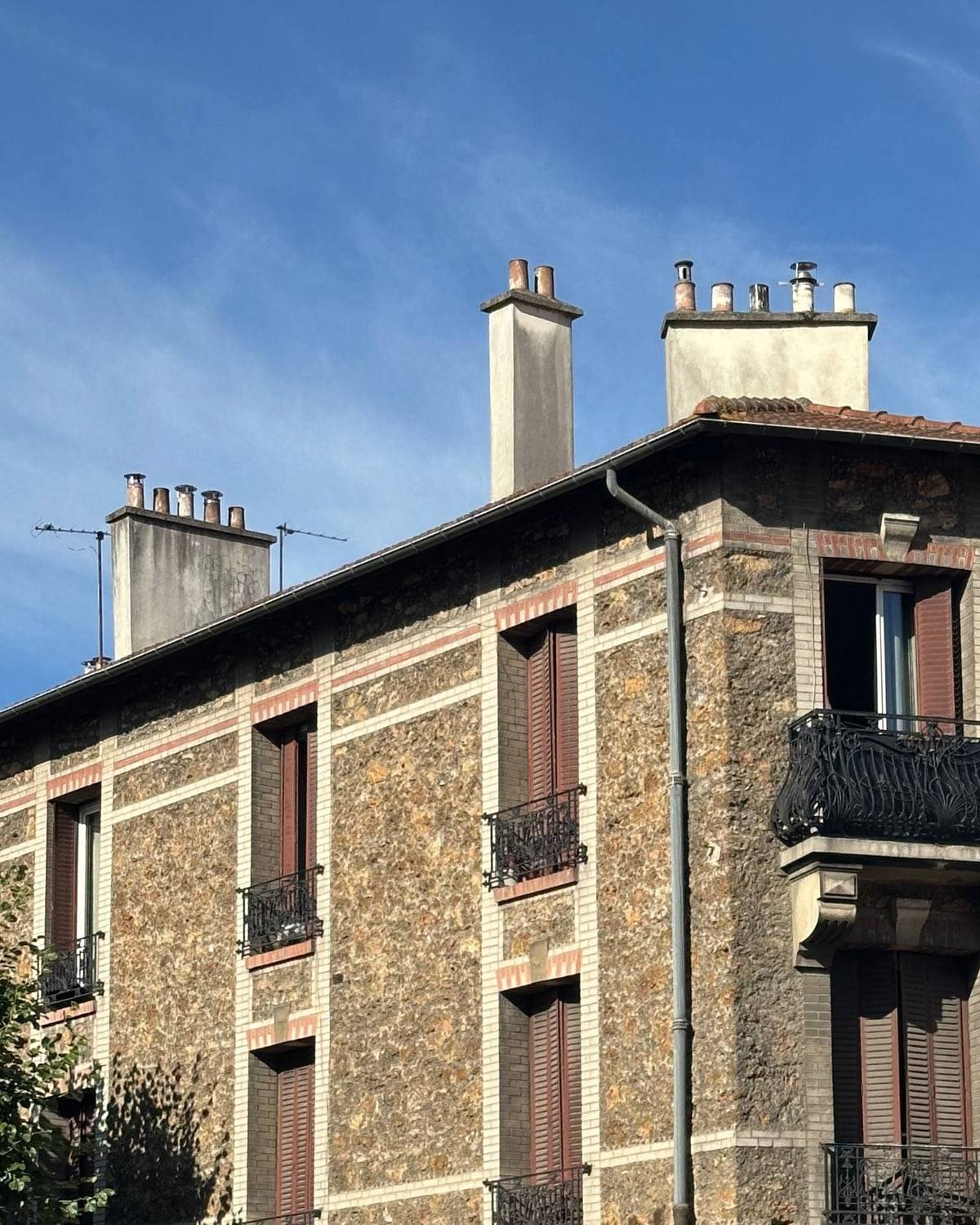 Un immeuble ancien en pierre meulière, balcons en fer forgé, sous un ciel bleu.